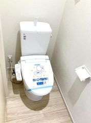 ホワイトで統一された温水洗浄便座付きトイレ。ホルダーやタオル掛けも完備され手入れがしやすい設計です。換気扇により清浄な空気を維持する、衛生的な環境が整えられた設備。窓を排したスッキリとした空間です