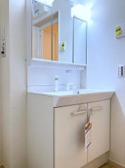 三面鏡の裏まで収納できる機能的な洗面台です。継ぎ目のないボウル形状は汚れが溜まりにくくお掃除も効率的。明るい照明が手元を照らし、朝の身支度もスムーズに行えるよう設計された、清潔感のある設備構成です